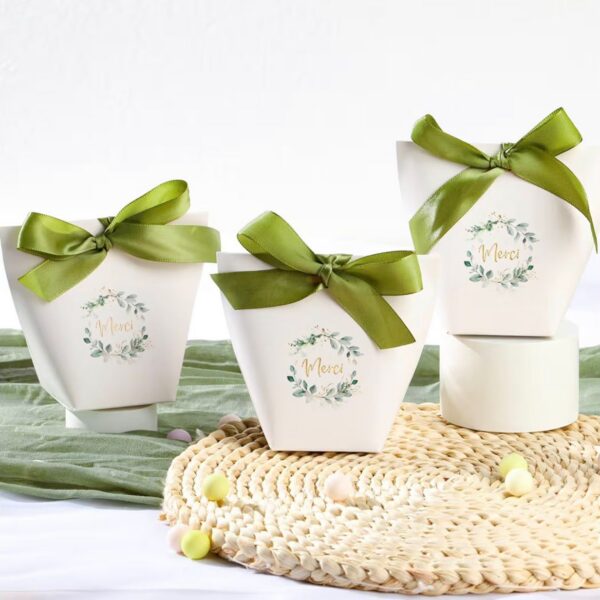 Trois boîtes cadeaux blanches de forme évasée avec une couronne de feuillage eucalyptus, l'inscription "Merci" et un large nœud en satin vert olive.