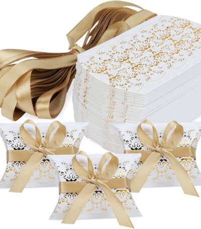 Lot d'emballages pour dragées en carton blanc avec motifs dorés élégants, forme coussin, accompagnés de rubans satinés dorés pour mariage et baptême.