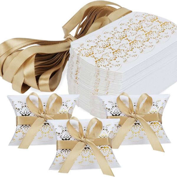 Lot d'emballages pour dragées en carton blanc avec motifs dorés élégants, forme coussin, accompagnés de rubans satinés dorés pour mariage et baptême.