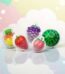 Assortiment de bonbons gélifiés en forme de fruits réalistes (Ananas, Fraise, Raisin, Pêche, Pastèque) présentés dans leurs coques individuelles, avec un cœur liquide fruité.