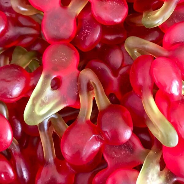 Gros plan sur un mélange de bonbons gélifiés en forme de cerises doubles rouges avec tiges vertes.