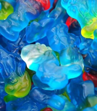 Gros plan sur un mélange de bonbons gélifiés bleus en forme de Schtroumpfs Haribo, translucides avec des bonnets de différentes couleurs.