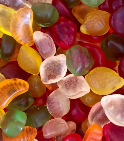 Assortiment de bonbons gélifiés sans sucre en forme de petits fruits multicolores (fraises, citrons, oranges) à texture translucide.