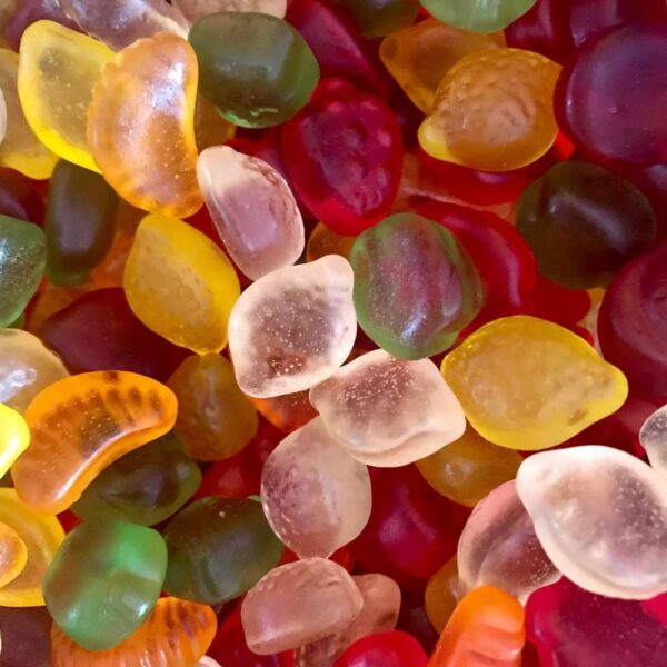 Assortiment de bonbons gélifiés sans sucre en forme de petits fruits multicolores (fraises, citrons, oranges) à texture translucide.