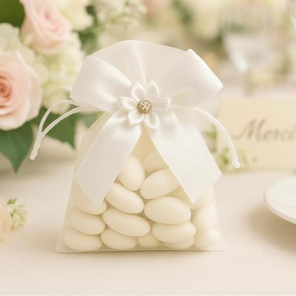 Sachet en organza blanc transparent rempli de dragées amandes blanches, décoré d'un nœud en satin, d'une fleur en tissu et d'un centre en strass.