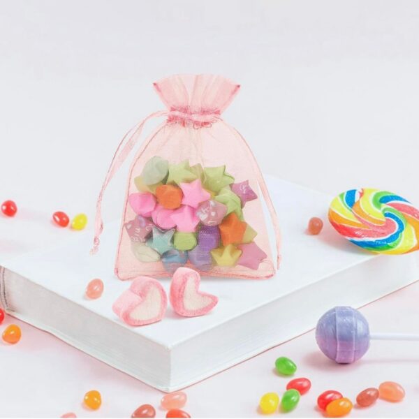 Sachet en organza rose translucide avec cordon de serrage, posé sur un livre blanc et rempli de petites étoiles en papier colorées.