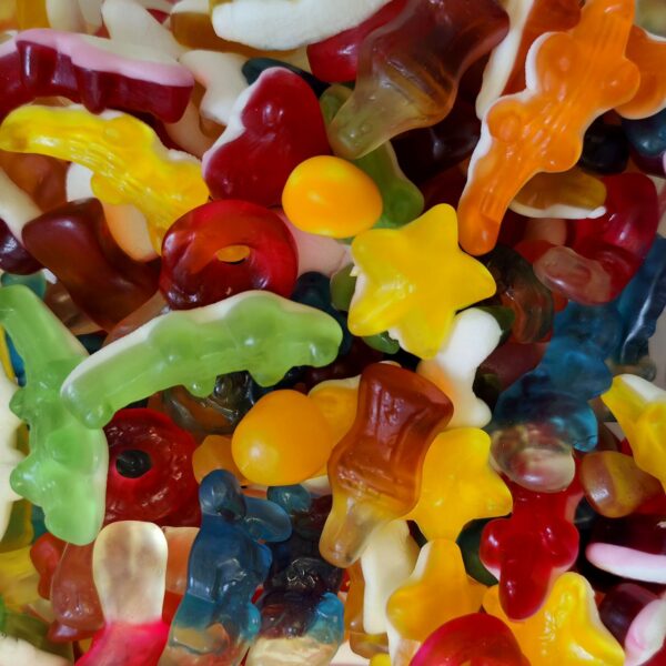 Vue de dessus d'un mélange coloré de bonbons : crocodiles gélifiés, bouteilles de cola, étoiles jaunes, cœurs rouges et anneaux fruités.