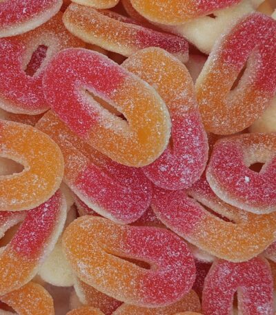 Gros plan sur des bonbons en forme d'anneaux bicolores orange et rouge, recouverts de sucre fin acidulé, les célèbres Rondelles Pêche de Trolli.