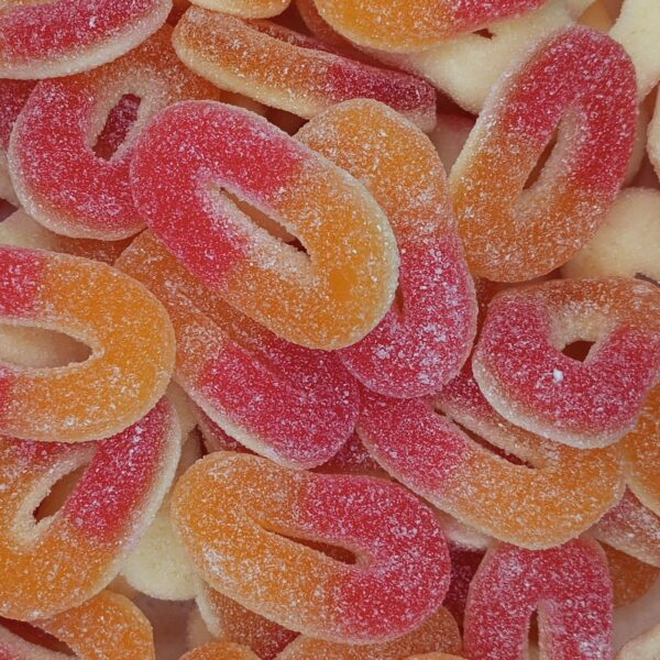 Gros plan sur des bonbons en forme d'anneaux bicolores orange et rouge, recouverts de sucre fin acidulé, les célèbres Rondelles Pêche de Trolli.